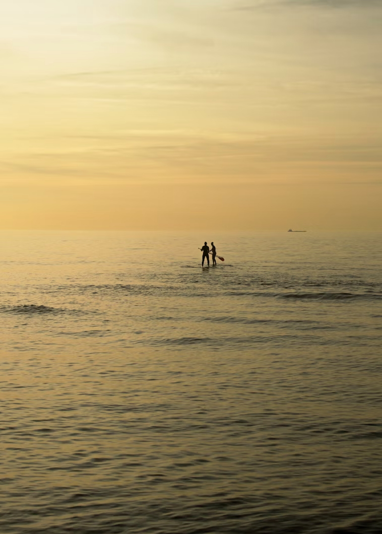 Deux hommes font du paddle sur une mer lors d'un coucher de soleil en Bretagne